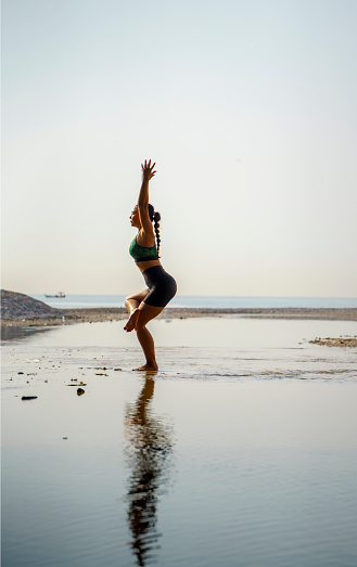 Woman practicing yoga on the beach at sunrise