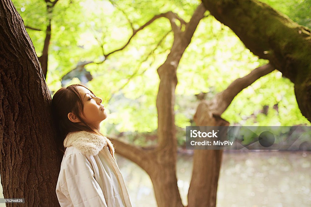 Enjoying nature Beautiful Japanese woman with closed eyes leaning up against a tree Adult Stock Photo