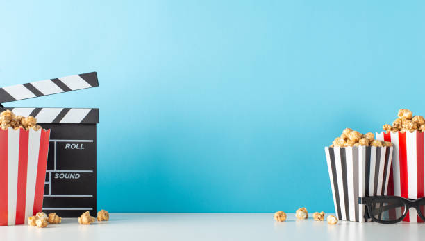 istock Elevate your film premiere using delightful snack motif. Capture side view of table featuring movie director's clapper, 3D specs, tasty popcorn against pastel blue backdrop, leaving space for movie ad 1752469485