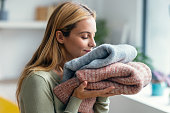 Beautiful young woman holding and smelling clean clothes at home.
