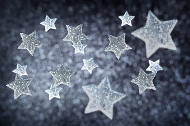 Shiny glittering christmas baubles or new year decoration of silver colour of star shape with sparkling sequins on blurred defocus black background with bokeh lights used for winter holiday design