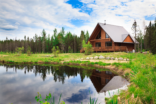 Large wood and stone log home surrounded by a cloudy sky and a lake.