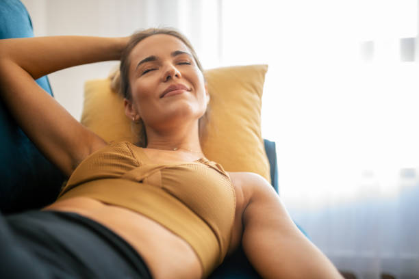 Beautiful young woman sleeping happy and with smile on sofa in living room. She is having a nap fully clothed. Apartment is bright and modern