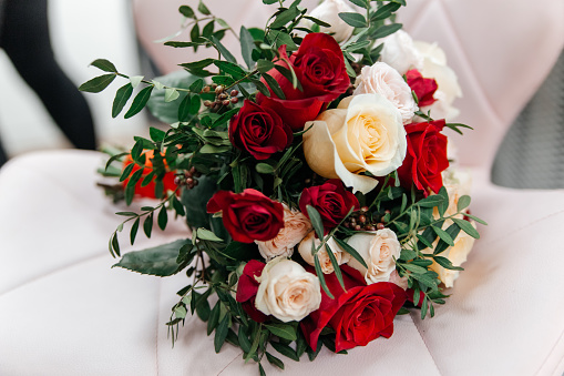 Delicate wedding bouquet of beige and red roses on a white leather armchair