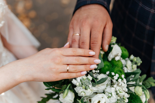 The hands of the bride and groom with rings on the background of the wedding white-green bouquet. The concept of marriage.