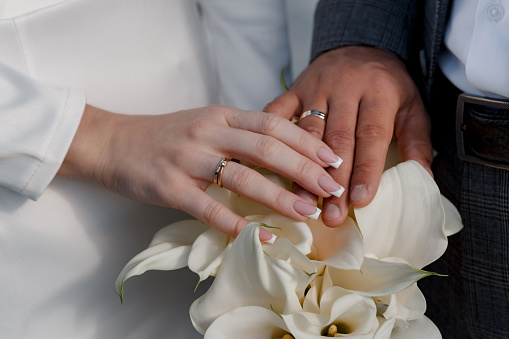 The hands of the bride and groom with rings on the background of a wedding bouquet of white calla lilies. The concept of marriage.