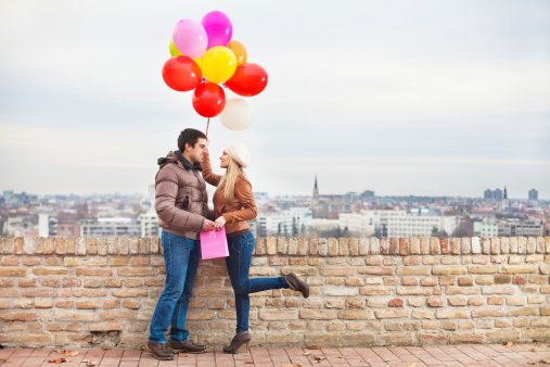 Happy couple with colorful balloons outdoors. View from a terrace to the city. Copy space