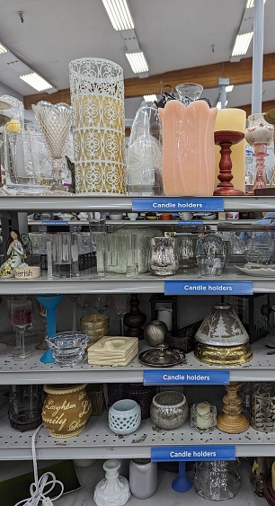 A collection of candle holders on display on labeled thrift store shelves.