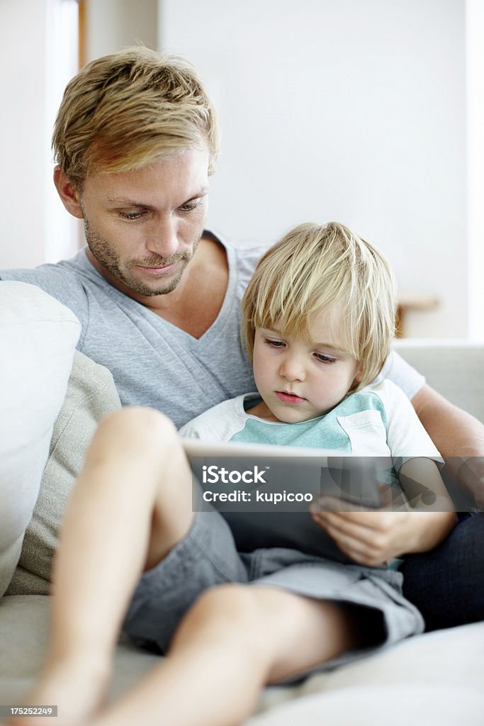 Getting to grips with technology together Loving father and son on the couch using their digital tablet together Adult Stock Photo