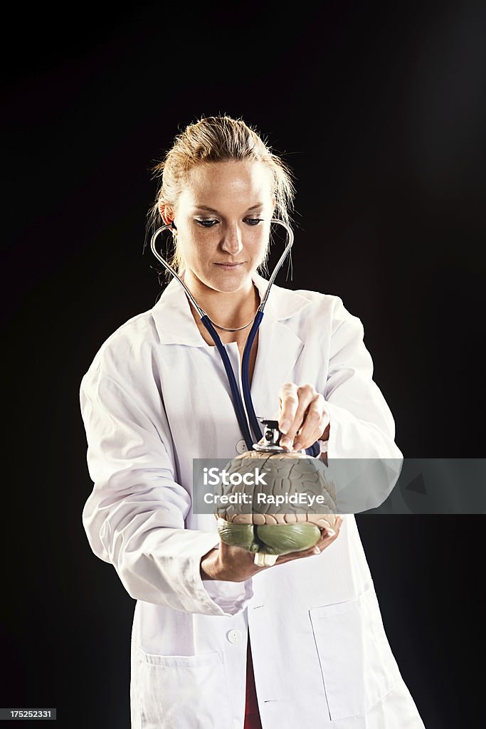 Giovane femmina medico Ascolta il modello cervello con Stetoscopio - Foto stock royalty-free di Adulto