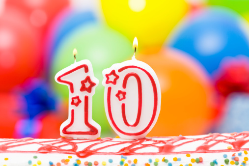 Cake for 10th birthday with lighted candles. Balloons in background.