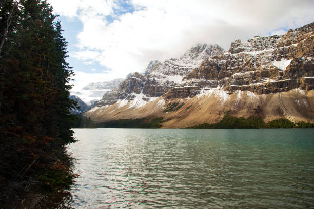 Mountains covered with snow above the lake with turquoise waters in a cold autumn day with cloudy sky. Bow lake, Banff national park, Canada.