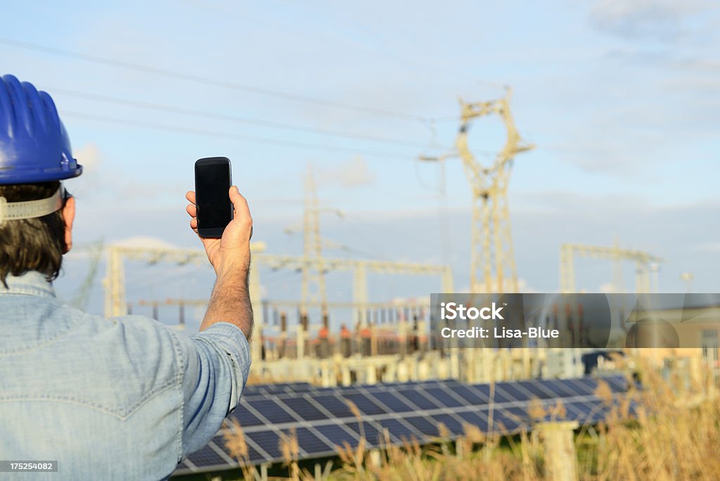 Ingegnere con Smart Phone in un impianto di energia solare - Foto stock royalty-free di Elmetto da cantiere