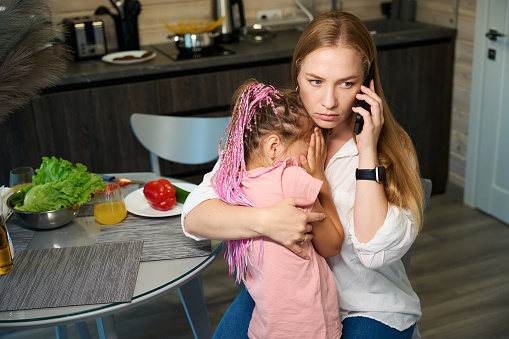 Anxious woman worrying about her little daughter who feeling sick, hugging and calming down child and calling emergency service