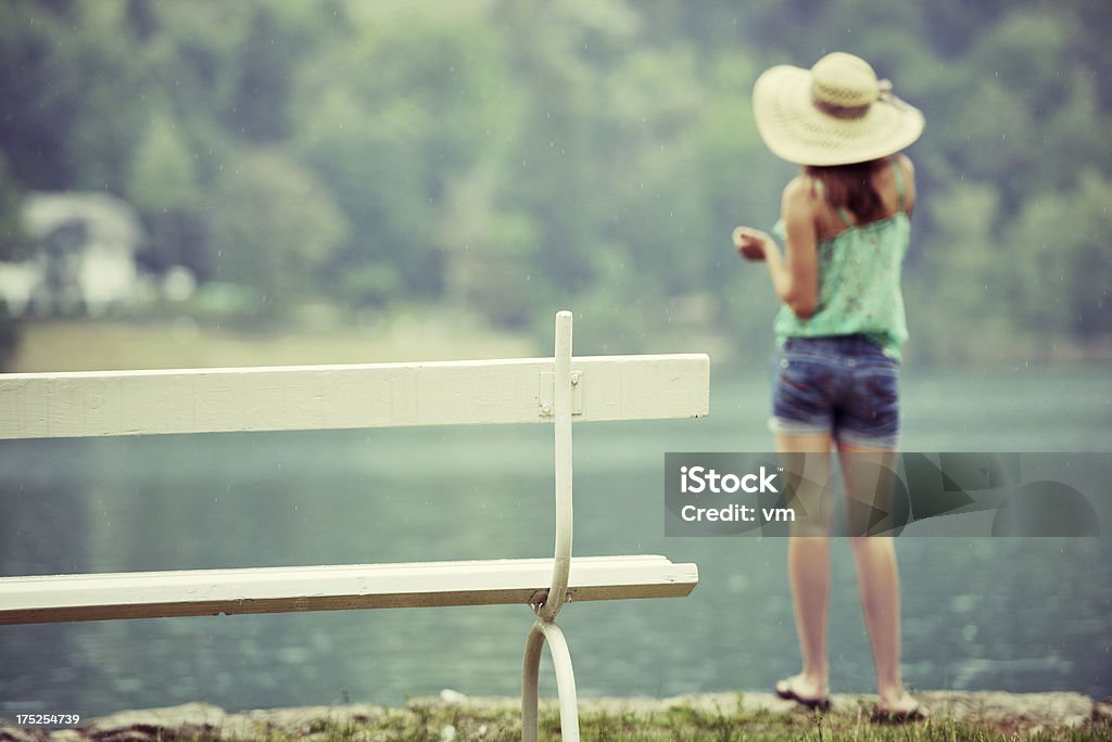 Giovane donna in piedi accanto a un lago - Foto stock royalty-free di Abbigliamento casual