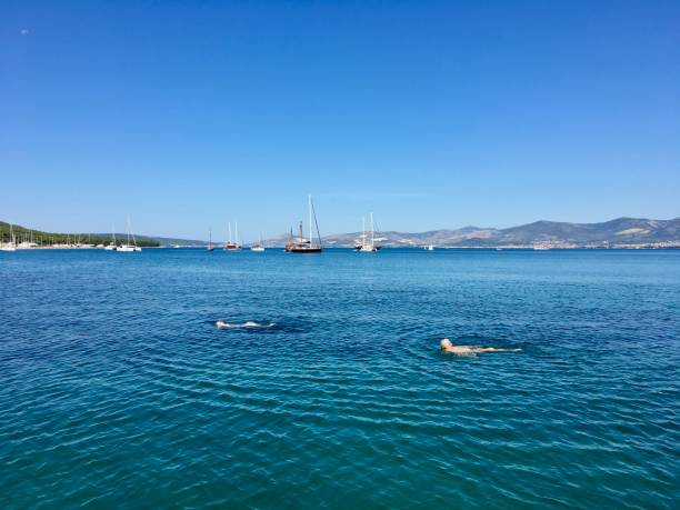 due persone che nuotano nel mare adriatico davanti a un piccolo porto turistico a spalato, croazia - horizon over land sports and fitness nature wave foto e immagini stock