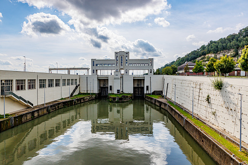 Front view of Lanaye lock with two small closed floodgates, Albert canal, building walls, bridge against gray blue sky, reflection on water surface, cloudy summer day in Ternaaien, Belgium