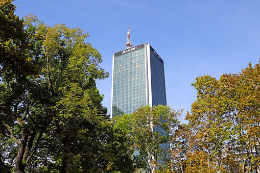 Warsaw, Poland - September 20, 2023: Above the treetops you can see the upper section of a tall building that houses the five-star Marriott Hotel in the city centre.
