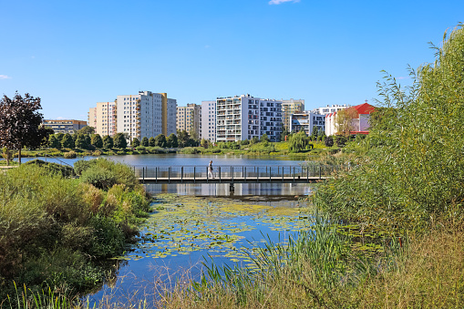 Warsaw, Poland - September 15, 2023: Residential buildings, lake, nature and footbridge seen on a sunny day as part of the Goclaw housing estate in the Praga-Poludnie district.
