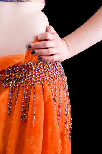 Vertical studio shot on black of womans side hip area with beaded belt holding scarf as skirt.