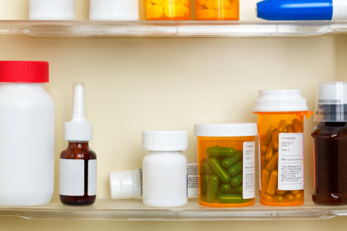 Several containers of over the counter and prescription medications on the shelves of a 1960's medicine cabinet.