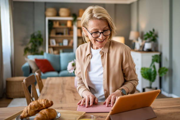 Portrait of a happy mature woman using a tablet at home while sitting at the kitchen island in her modern apartment stock photo