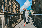 Outdoor autumn portrait of young elegant fashionable woman wearing trendy sunglasses, gray color coat, black jeans and turtleneck walking on street of European city in sunny day. street style fashion.