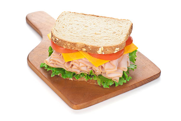 Deli Style Turkey Sandwich on Cutting Board "Whole deli turkey (or chicken) sandwich; with Cheddar cheese, tomatoes, lettuce, and whole grain bread, on a cutting board." turkey breast stock pictures, royalty-free photos & images