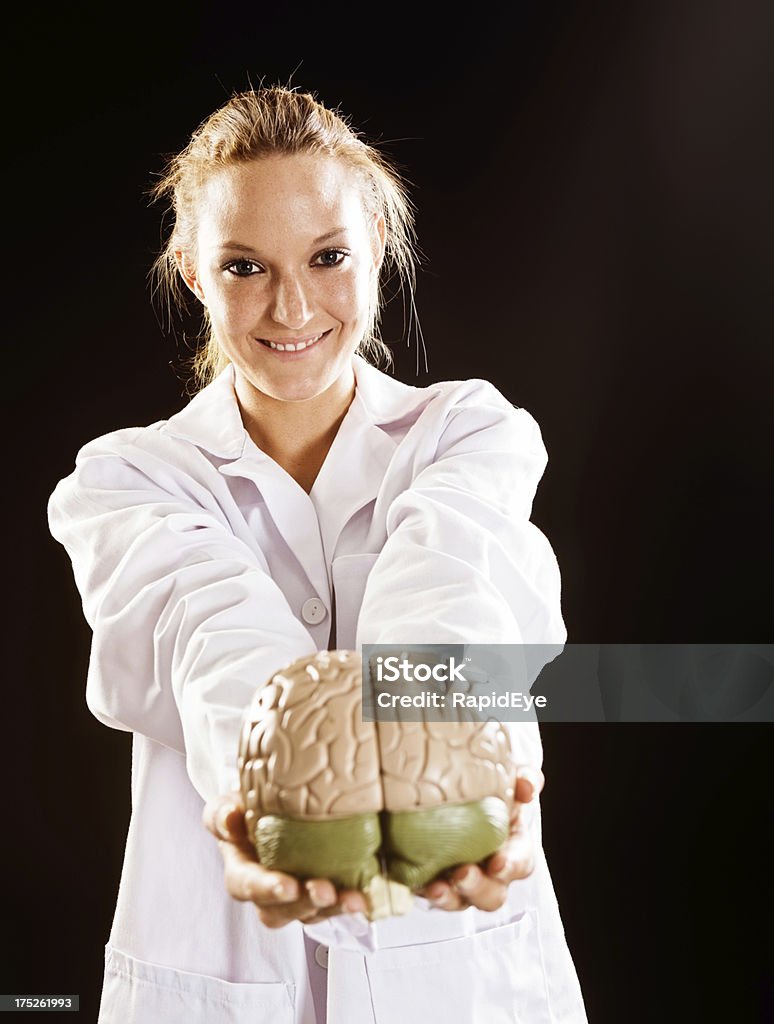 Something to think about! Smiling woman doctor offers model brain "A pretty young blonde doctor holds out an anatomical model of the human brain, smiling." Adult Stock Photo