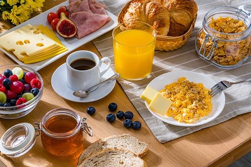 Healthy breakfast of scrambled eggs, cheese, ham, coffee, croissants and fruit juice