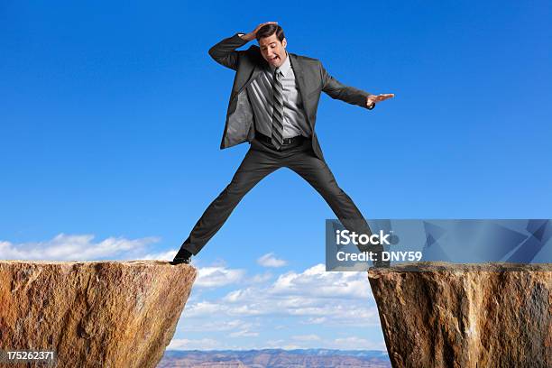 Businessman Straddling The Divide Created By Two Cliffs Stock Photo - Download Image Now