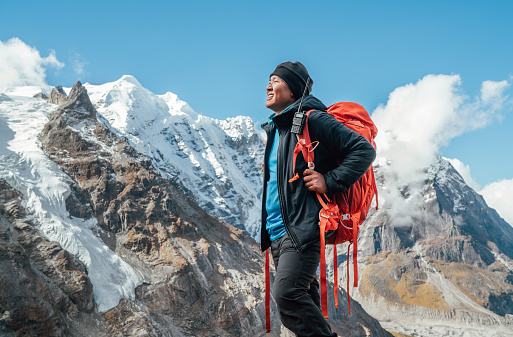 Portrait of smiling Sherpa man with backpack enjoying mountain views and fresh air with Mera peak 6476m background. High Himalayas expedition during mount climbing. Traveling and active people concept
