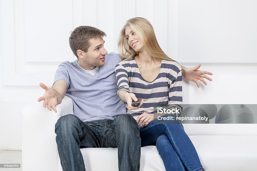 Joven caucásica pareja sentada en un sofá de retención de control remoto - Foto de stock de 20-24 años libre de derechos