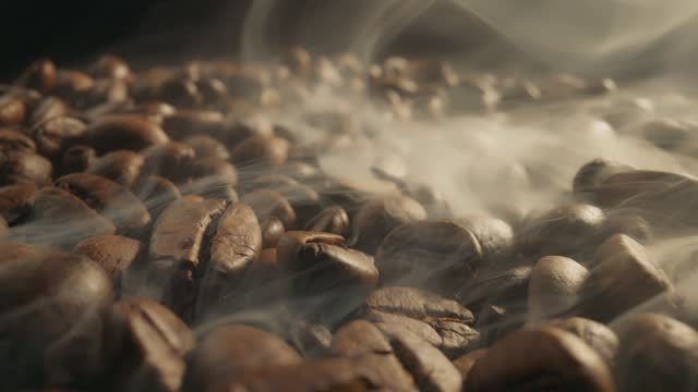 Roasting coffee beans with smoke on dark background. Smoke comes from fresh coffee seeds. Slider Macro shot, 4K