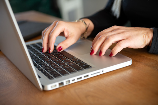 Woman hand typing on laptop and holding a cup of coffee at home office