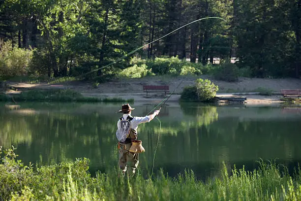 Fly fisherman working Fawn Lakes, on the Red River in Northern New Mexico. 3/4 rear view of fisherman and partially backlit. Some motion blur of pole, line, and arm