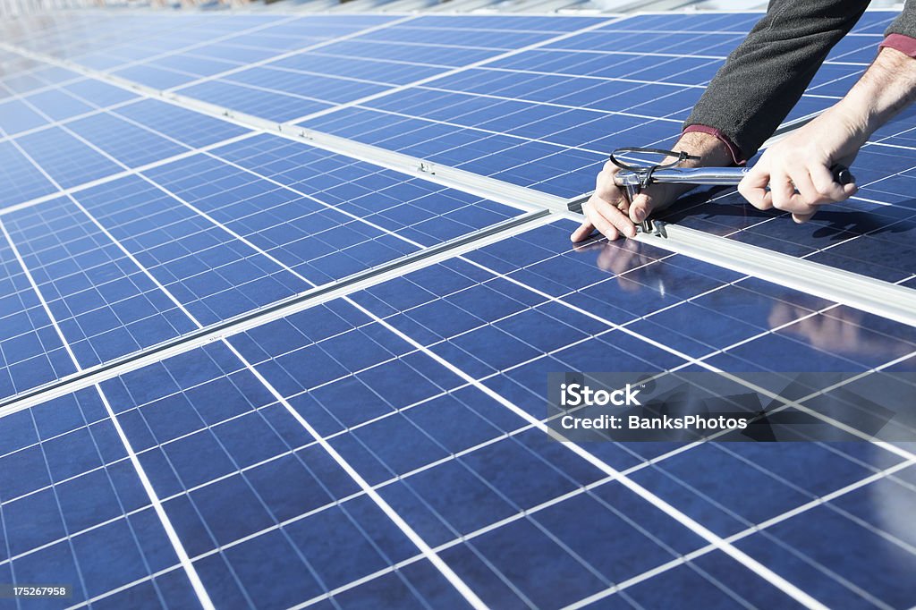 Solar Panel Installing with Torque Wrench A worker is using a torque socket wrench to install a solar panel onto a building's roof. The reflection on the lower right is a hard hat from another worker. Solar Panel Stock Photo