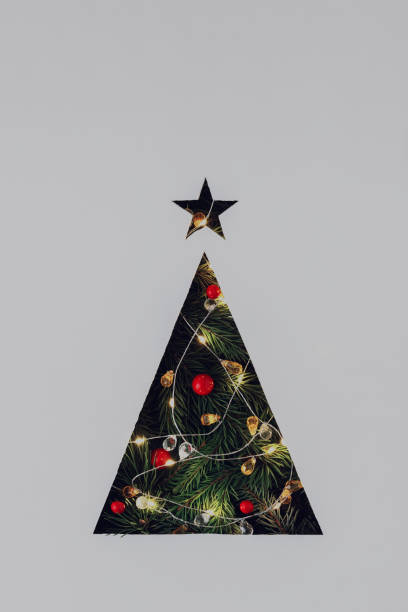 istock Triangular Christmas tree cut out in gray cardboard with lighted garland and Christmas tree branches. 1752681236