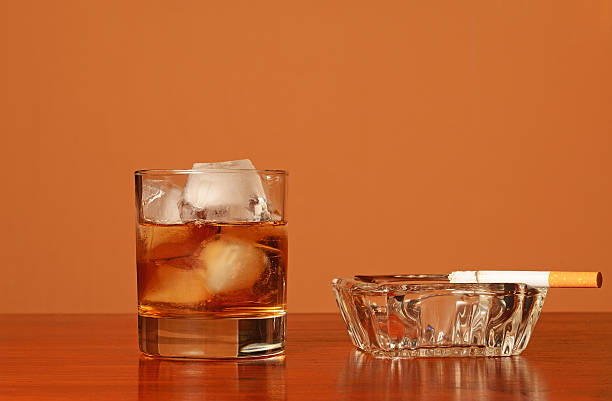 Glass of wiskey on the rocks and ashtray with cigarette stock photo