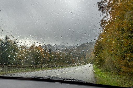 Raindrops on the glass. Bright autumn road. Raindrops on the windshield of the car. Gloomy autumn weather. Rainy season. Road trip. Fall colors.