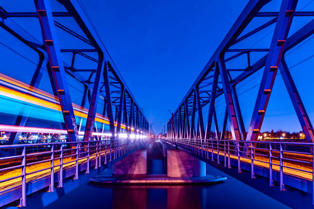 Two symmetrical steel railway bridges at night with train light trail on the left. Stars on the sky. Long exposure photo.