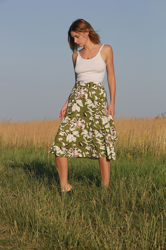 Candid outdoor portrait on the meadow of young woman linen skirt and white top. Casual summer fashion.