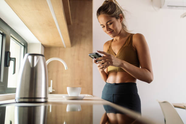 istock Young woman preparing tea in kitchen using electric kettle and using mobile phone 1752723337