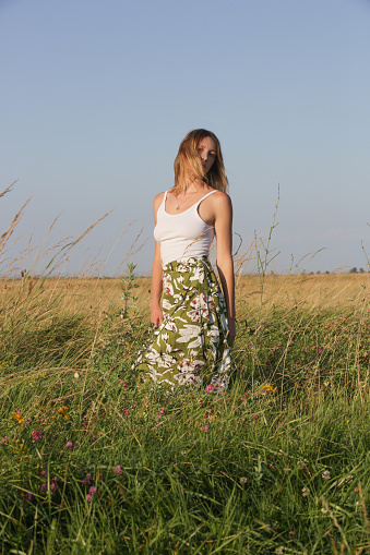 Candid outdoor portrait on the meadow of young woman linen skirt and white top. Casual summer fashion.