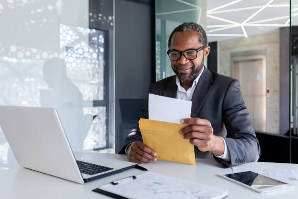 istock Senior satisfied financier received a letter mail message in an envelope, businessman reads and smiles, boss at desk inside office uses laptop 1752732290