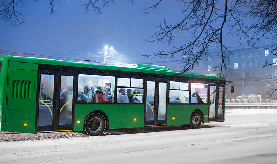 Bus moves along the city street on a winter evening in the snow.