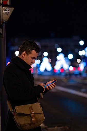 Young Latin boy with mobile phone with a night and urban background at Christmas and winter in Spain