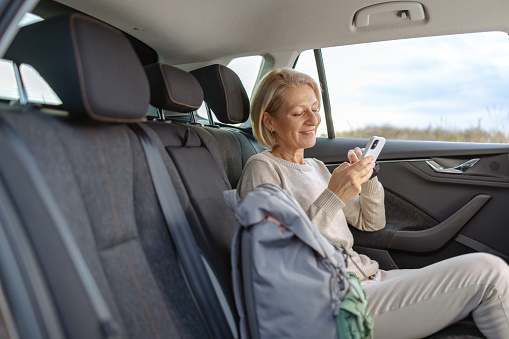 Smiling mature woman with blond hair is sitting on back seat of car and enjoying the ride
