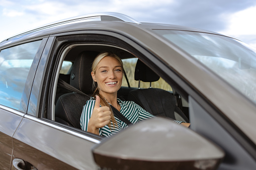 An attractive blond-haired woman sitting in the driver's seat of an electric car. She is smiling and looking at the camera