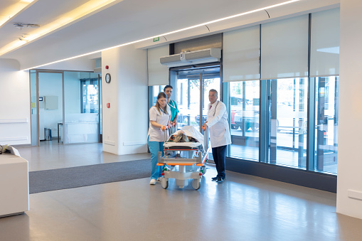 The paramedics take the patient from the ambulance to the hospital on a stretcher. Two paramedics and a patient. Modern ambulance. Emergency room entrance of a large hospital.